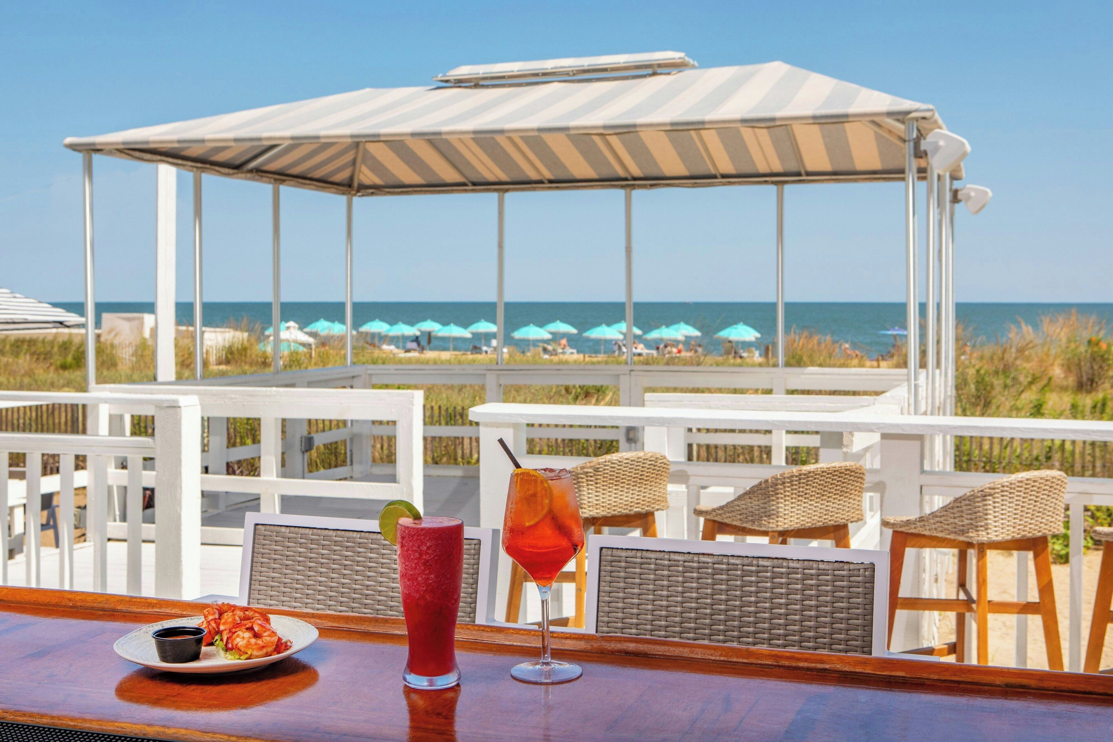 Un bar sulla spiaggia con vista sull'oceano, sedie in vimini e una zona con tettoia.