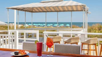 A beachside bar with a view of the ocean, wicker chairs, and a covered seating area.
