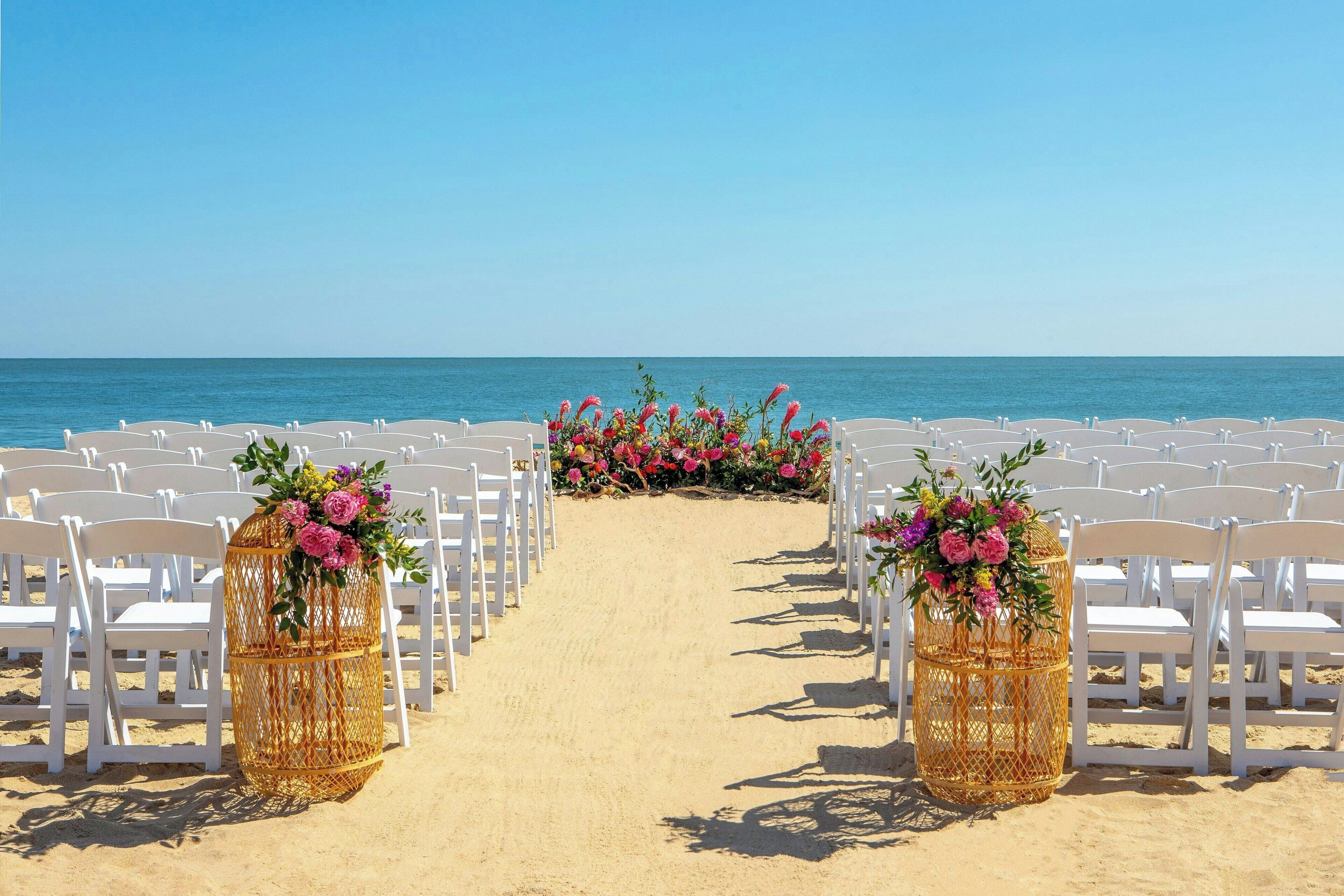 A beach wedding aisle with white chairs and wicker flower stands.