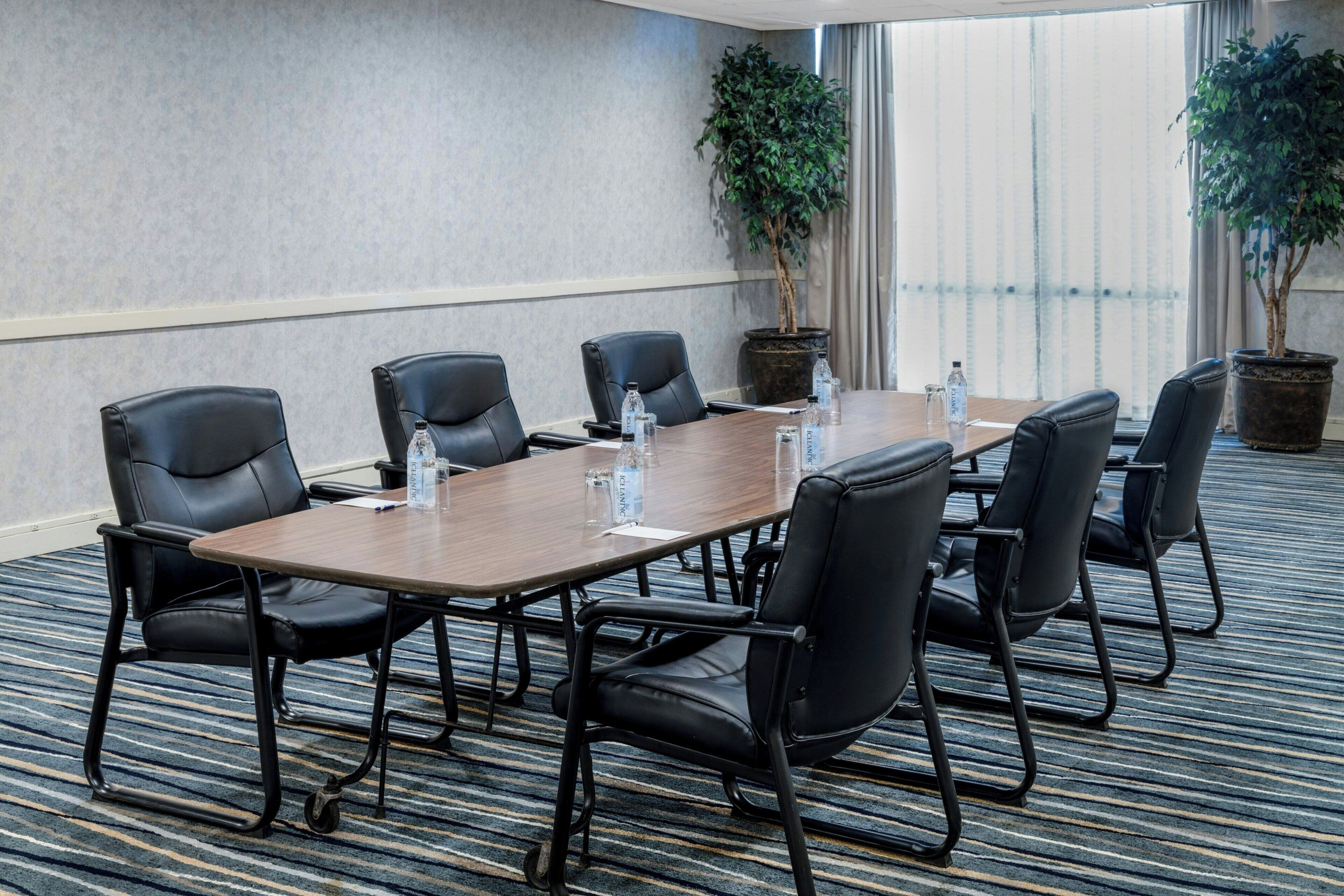 A conference room with a long table, black leather chairs, potted plants, and a carpeted floor.