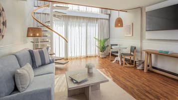 A modern living room with a sofa, coffee table, TV, and a staircase.