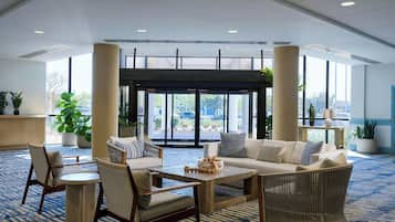 A lobby with a seating area, large windows, and a view of the outside.