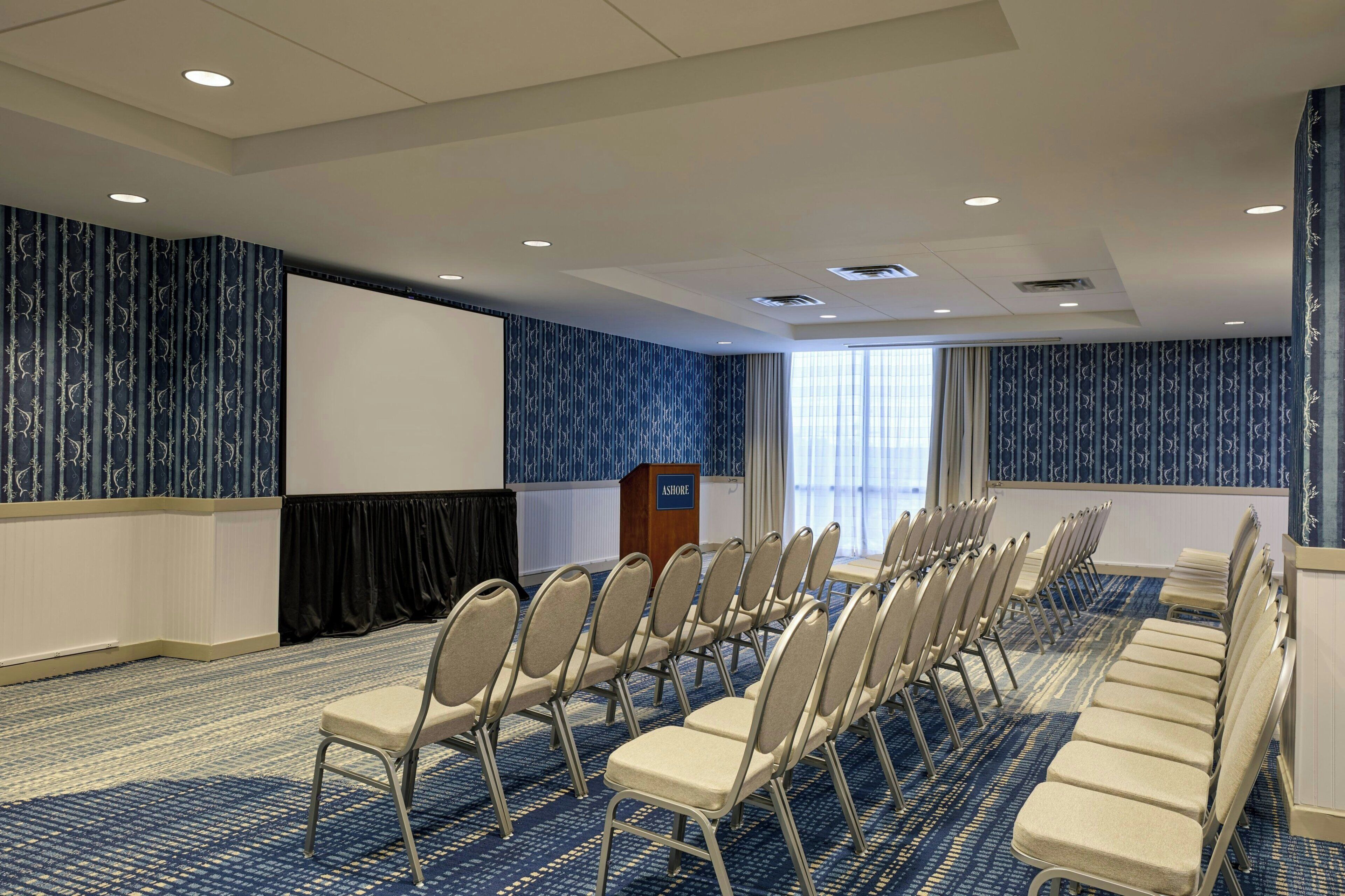 A conference room with rows of chairs, a podium, and a large screen.