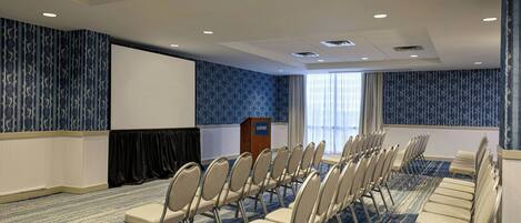 A conference room with rows of chairs, a podium, and a large screen.