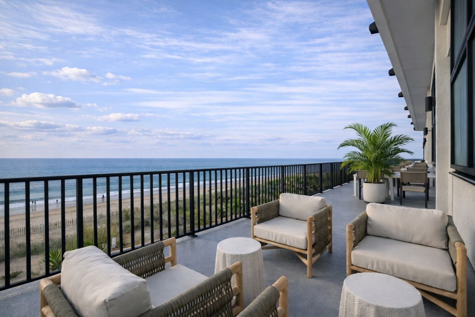 A balcony with wicker furniture, a view of the beach, and a potted plant.