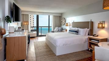 A modern hotel room with a large bed, a desk, a TV, and a balcony with a view.