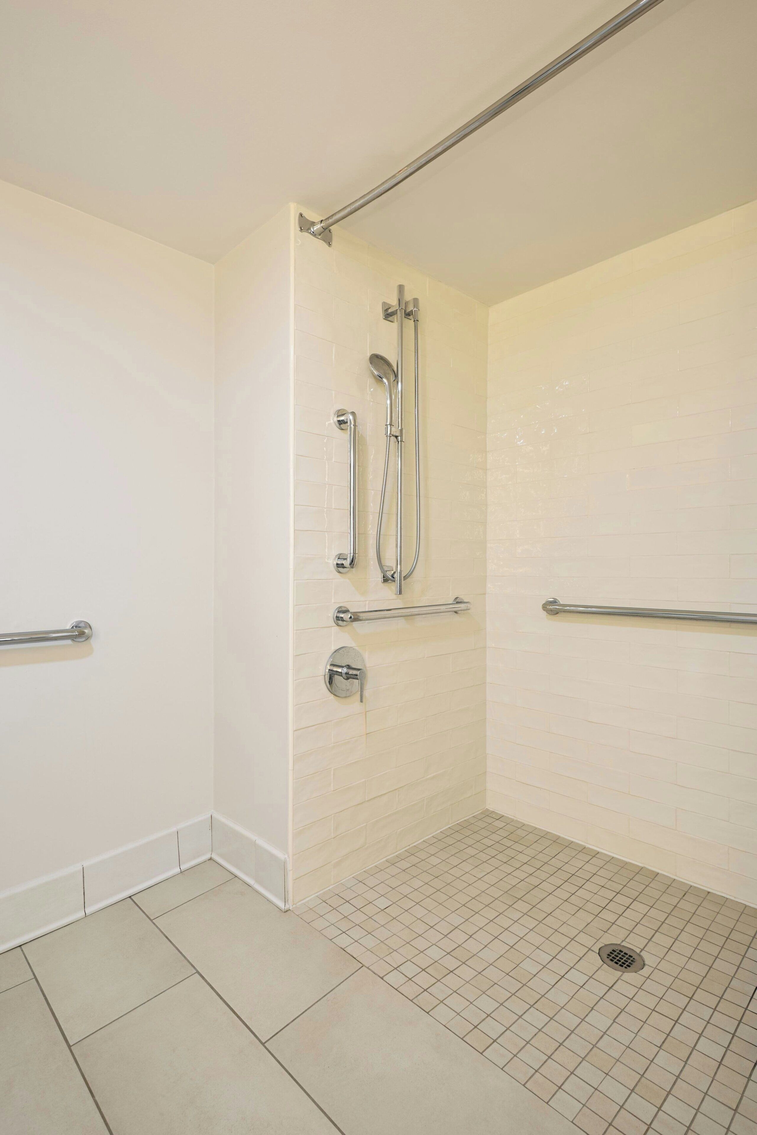 A bathroom with white tiled walls, a shower with grab bars, and a tiled floor.