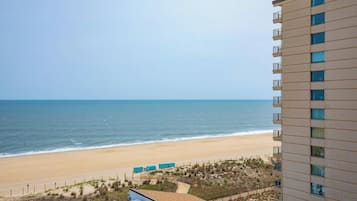 A beachfront hotel with a view of the ocean, a sandy beach, and a parking area with several air conditioning units.