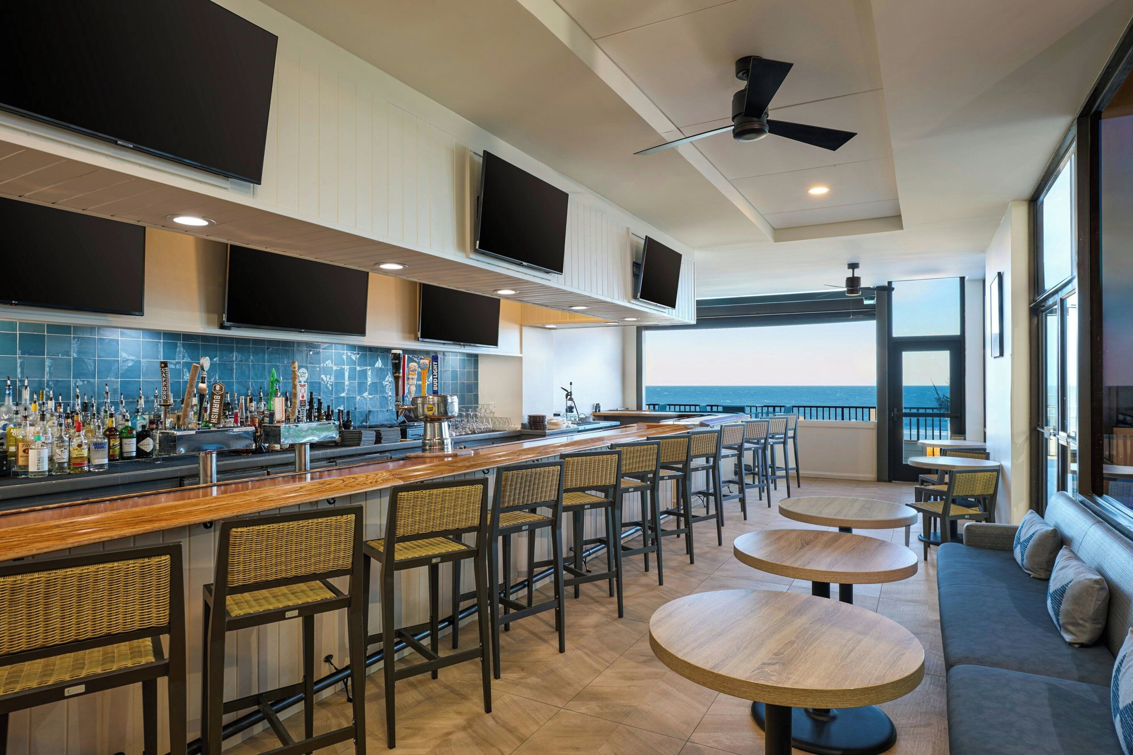 A bar area with a long counter, multiple screens, and seating with a view.