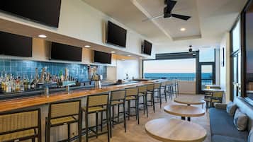 A bar area with a long counter, multiple screens, and seating with a view.