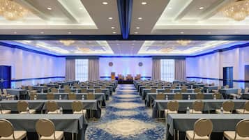 A conference room with rows of tables and chairs, a stage with podiums, and chandeliers.