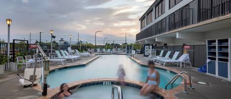 A swimming pool with lounge chairs and a building with balconies.