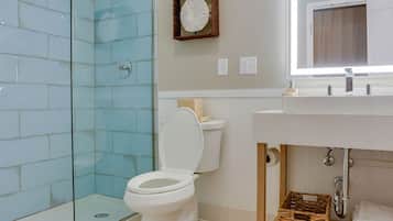 Un baño moderno con cabina de ducha de vidrio, inodoro blanco y tocador de madera con espejo sobre el lavabo.