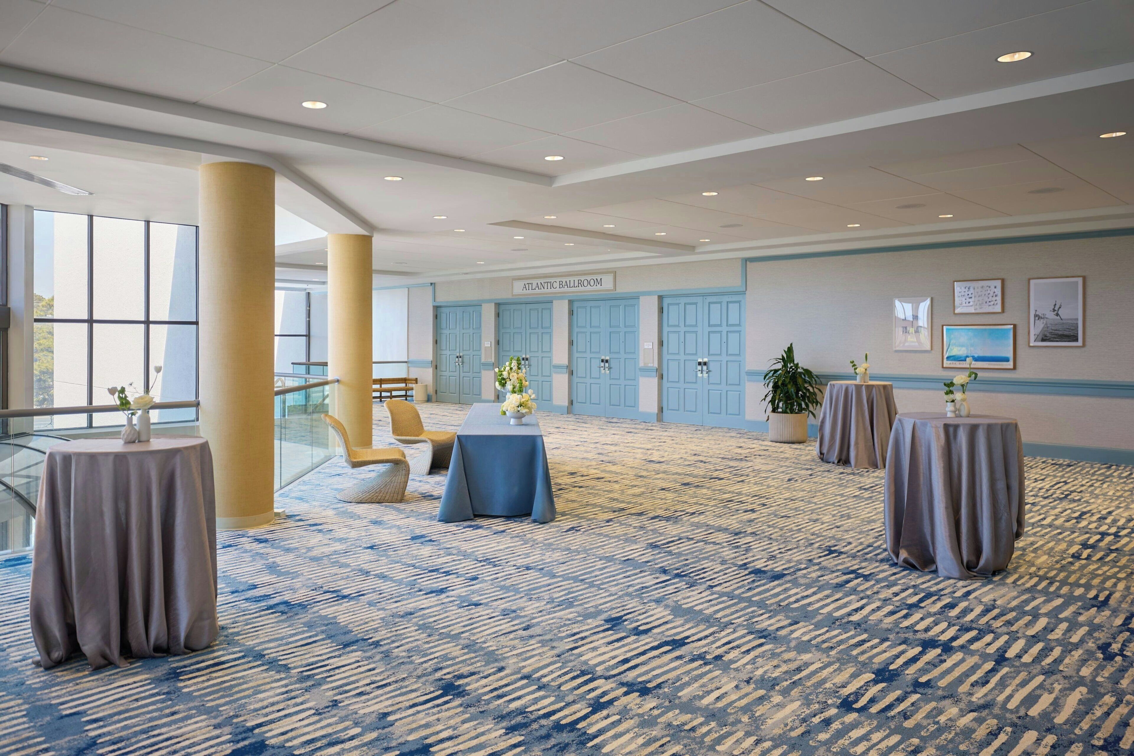 Una habitación amplia con alfombra azul, una mesa con un jarrón de flores y un cartel que dice 'ATLANTIC BALLROOM'.