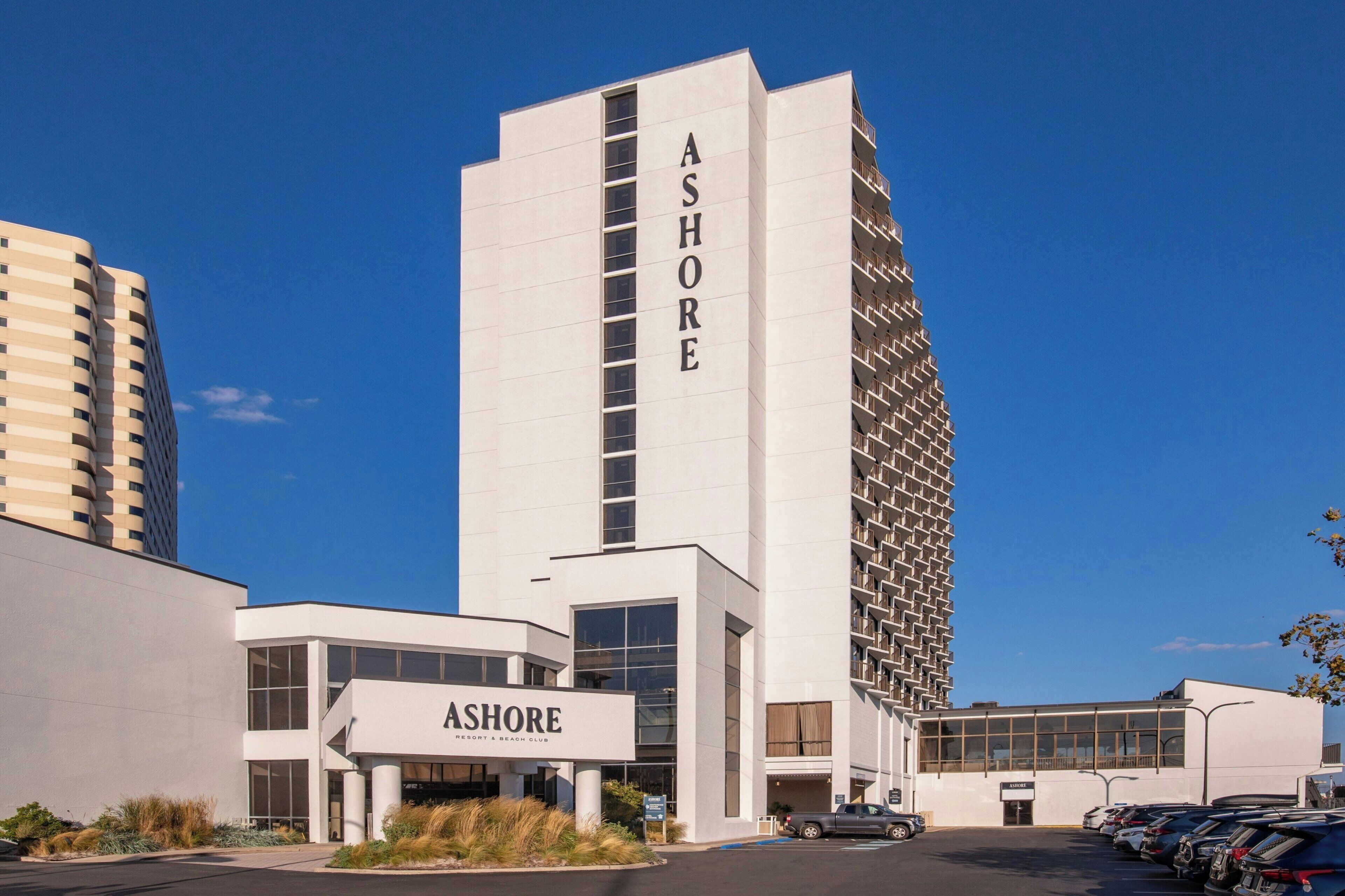 A modern building with 'ASHORE' signage, a parking lot, and a clear blue sky.