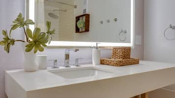 A modern bathroom with a large mirror, white sink, and a decorative woven stool.