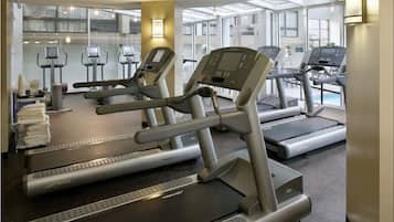 Un gimnasio con varias cintas de correr, bicicletas estáticas y un espejo grande.