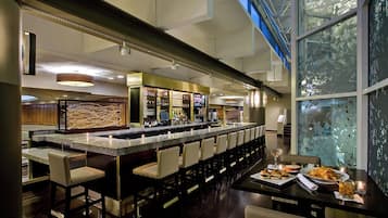A bar area with a long counter, multiple bar stools, and a television screen.
