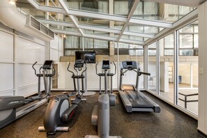 Een moderne fitnessruimte met diverse cardioapparaten, grote ramen en een hoge plafond.