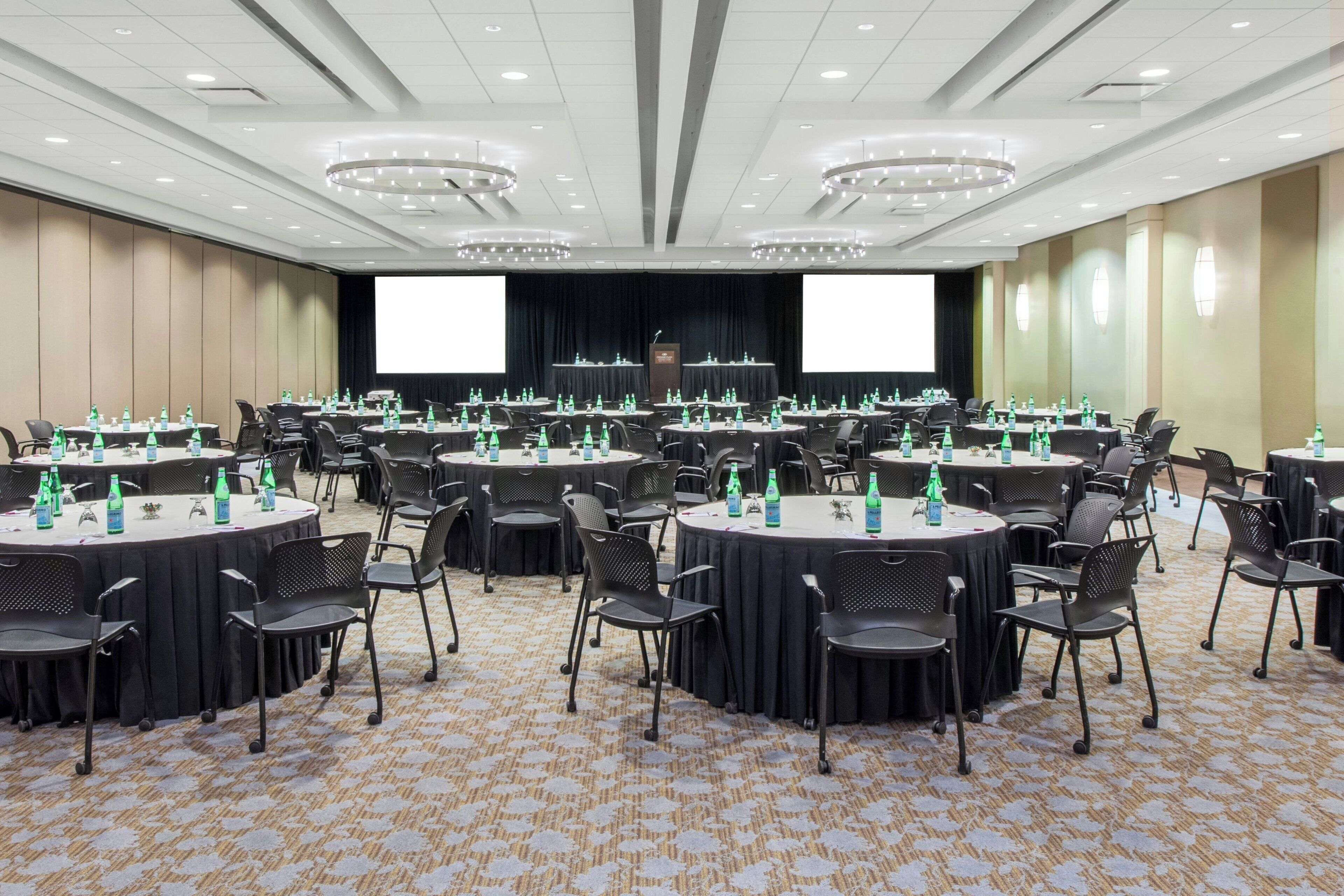 A conference room with multiple round tables, each with chairs and water bottles.