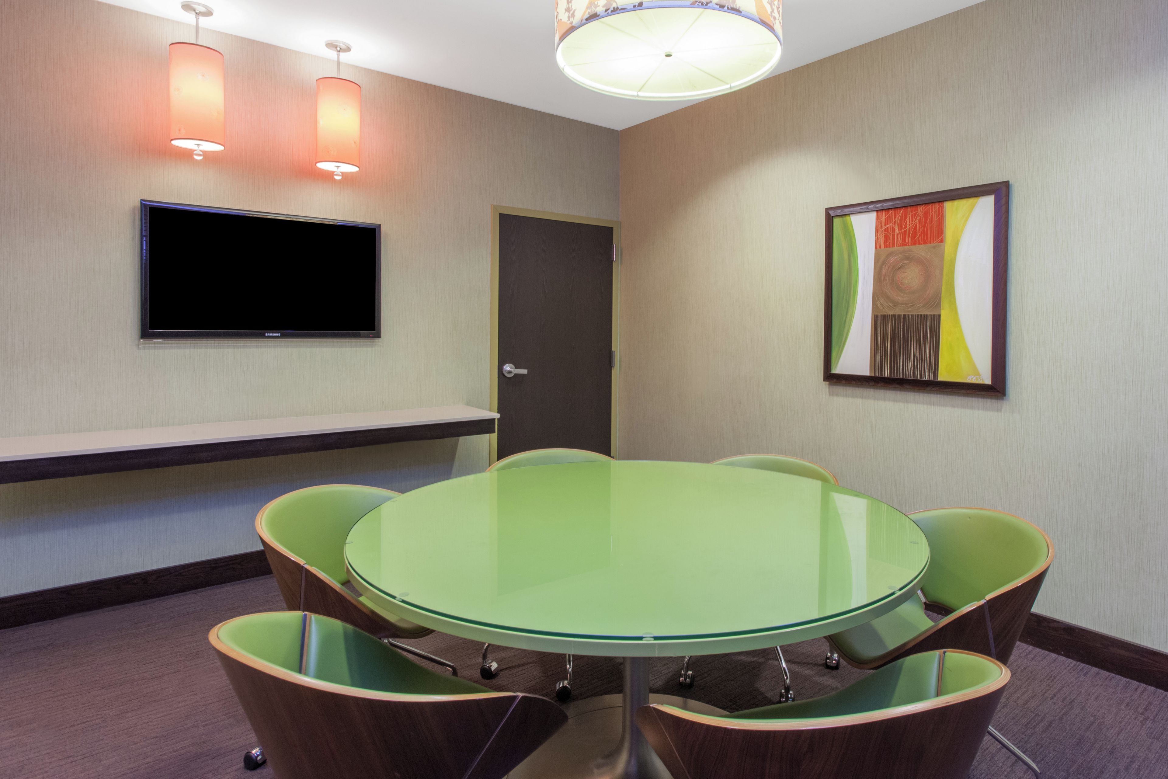 A conference room with a glass table surrounded by chairs, a flat-screen TV mounted on the wall, and a door with a handle.