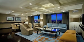 Una habitación de hotel con zona de comedor, sofá, mesa de centro y televisor.