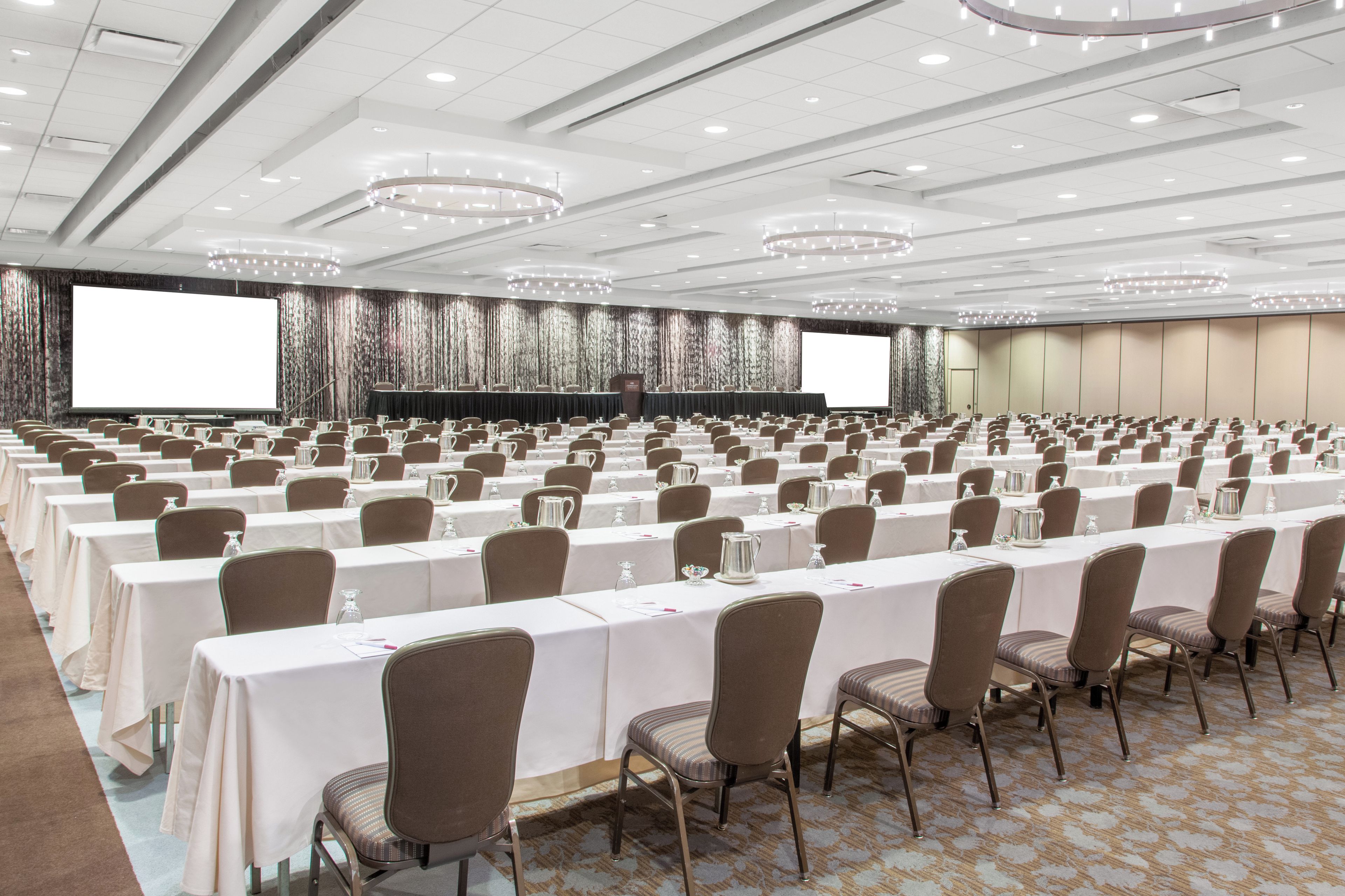 A conference room with rows of tables and chairs, a large screen, and a stage with a podium.