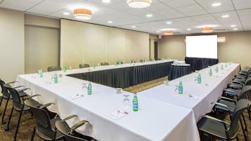 Un salón de conferencias con una larga mesa, sillas y una pantalla de proyector.