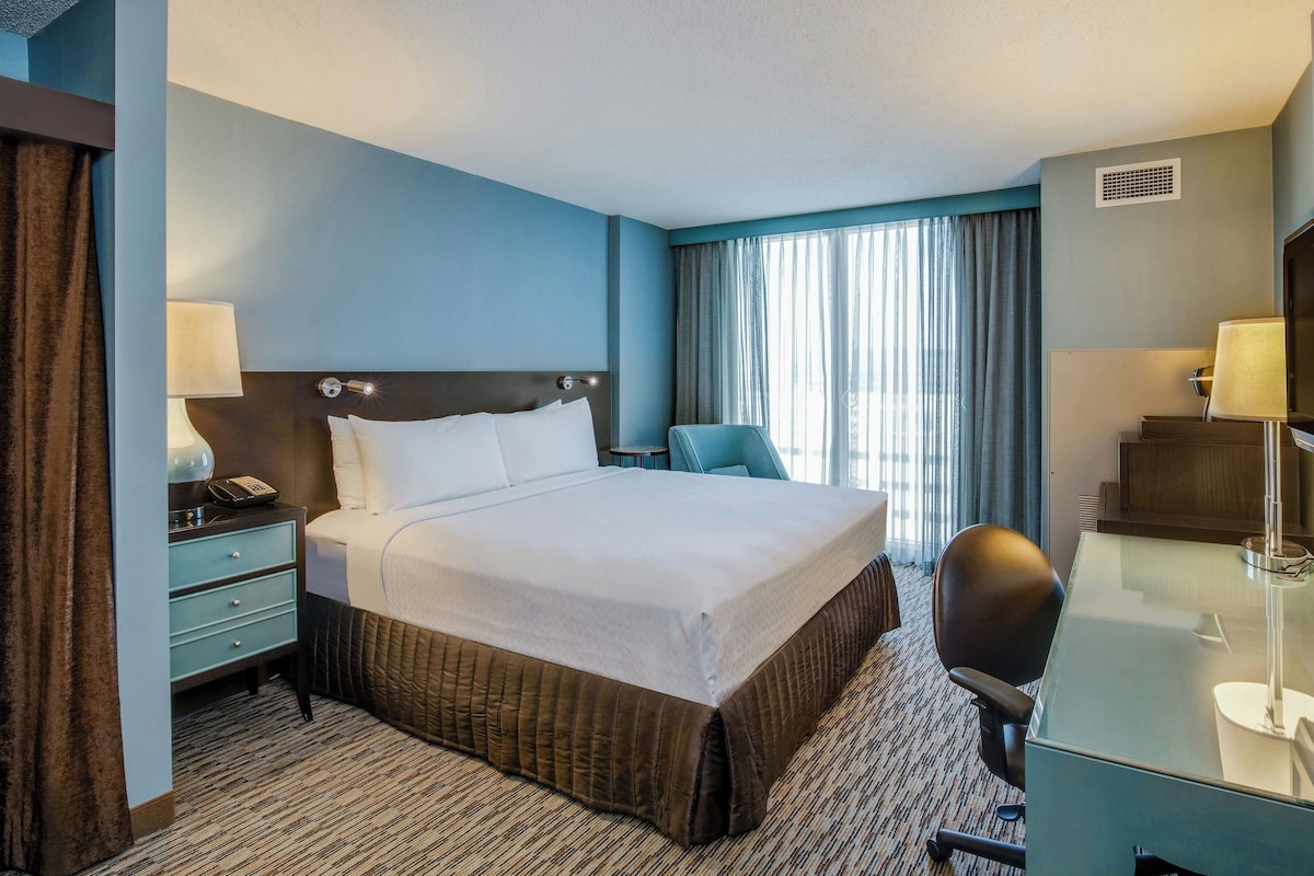 A hotel room with a bed, desk, chair, and a window with curtains.