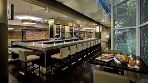Un espace bar moderne avec un long comptoir, des tabourets de bar et un écran de télévision.