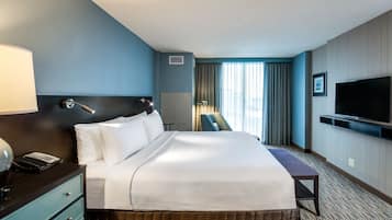 Una habitación de hotel con cama, escritorio, silla, televisión y ventana con cortinas.