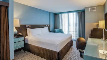 Habitación de hotel con cama, escritorio, silla y cortinas.