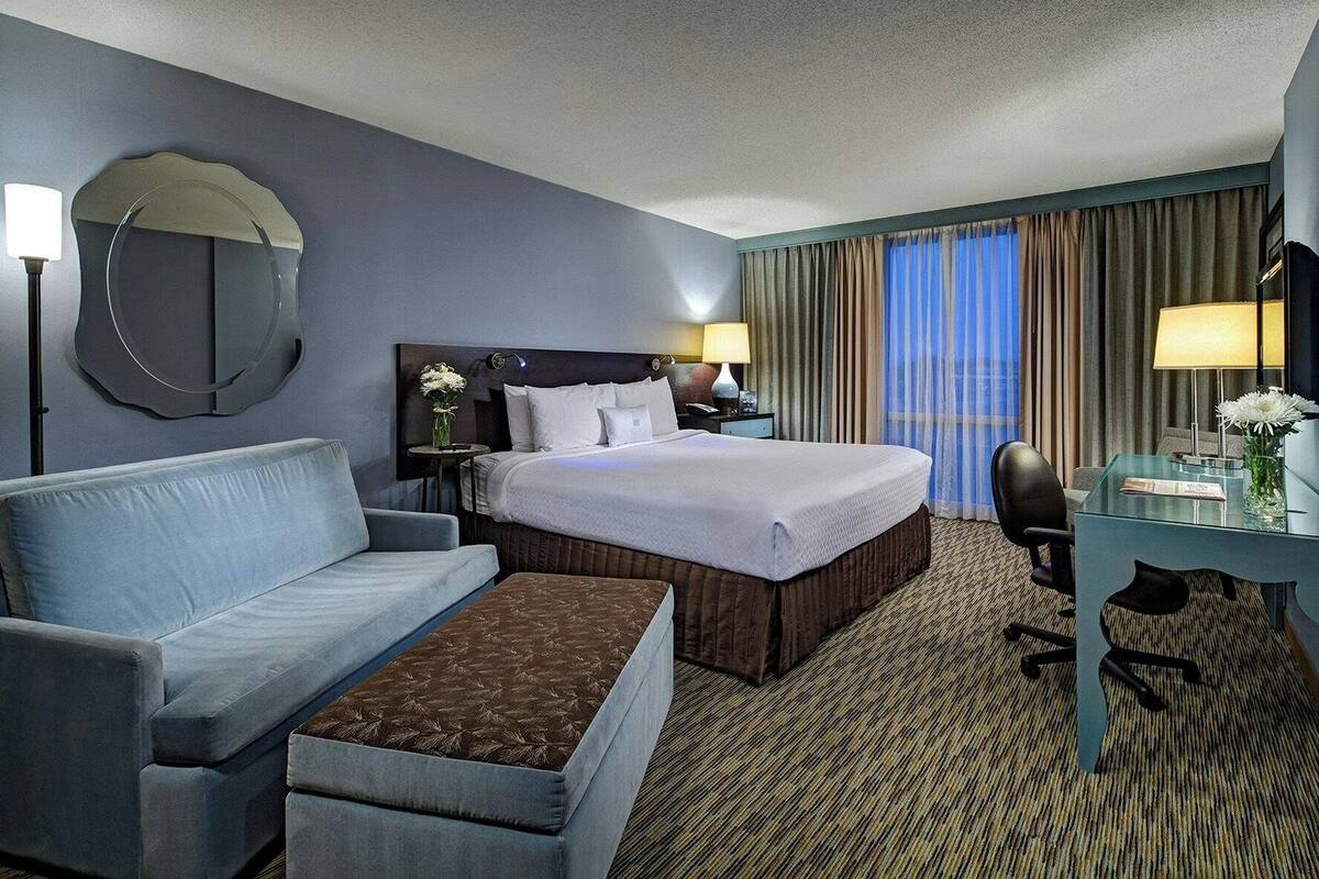 Une chambre d’hôtel comprenant un lit, un canapé, un bureau, une chaise, une lampe, un miroir et une fenêtre avec des rideaux.