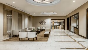 Un hall d’hôtel spacieux, doté d’un long comptoir d’accueil, d’un espace salon avec des canapés et des fauteuils, et d’un lustre moderne.