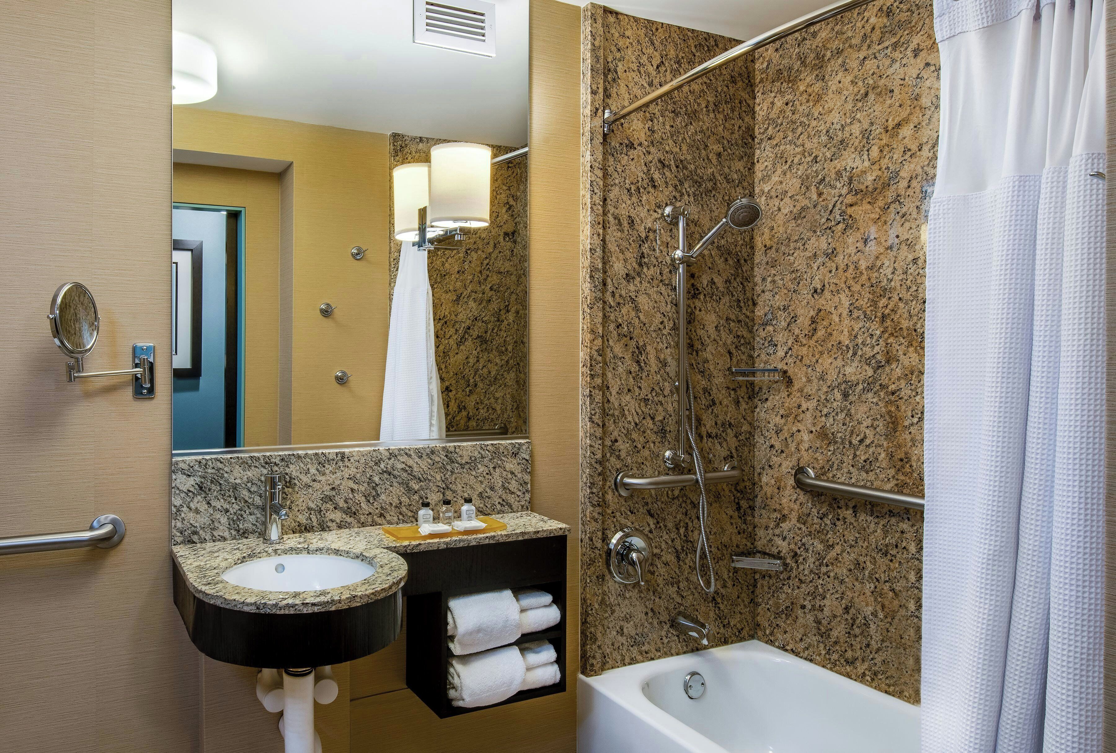 A bathroom with a granite countertop sink, a mirror, a shower with a handheld showerhead, and a bathtub.