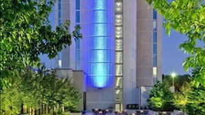 Un hôtel reconnaissable à son grand panneau « Crowne Plaza », doté d’une façade moderne et d’un espace extérieur bien entretenu, agrémenté de sièges et de verdure.