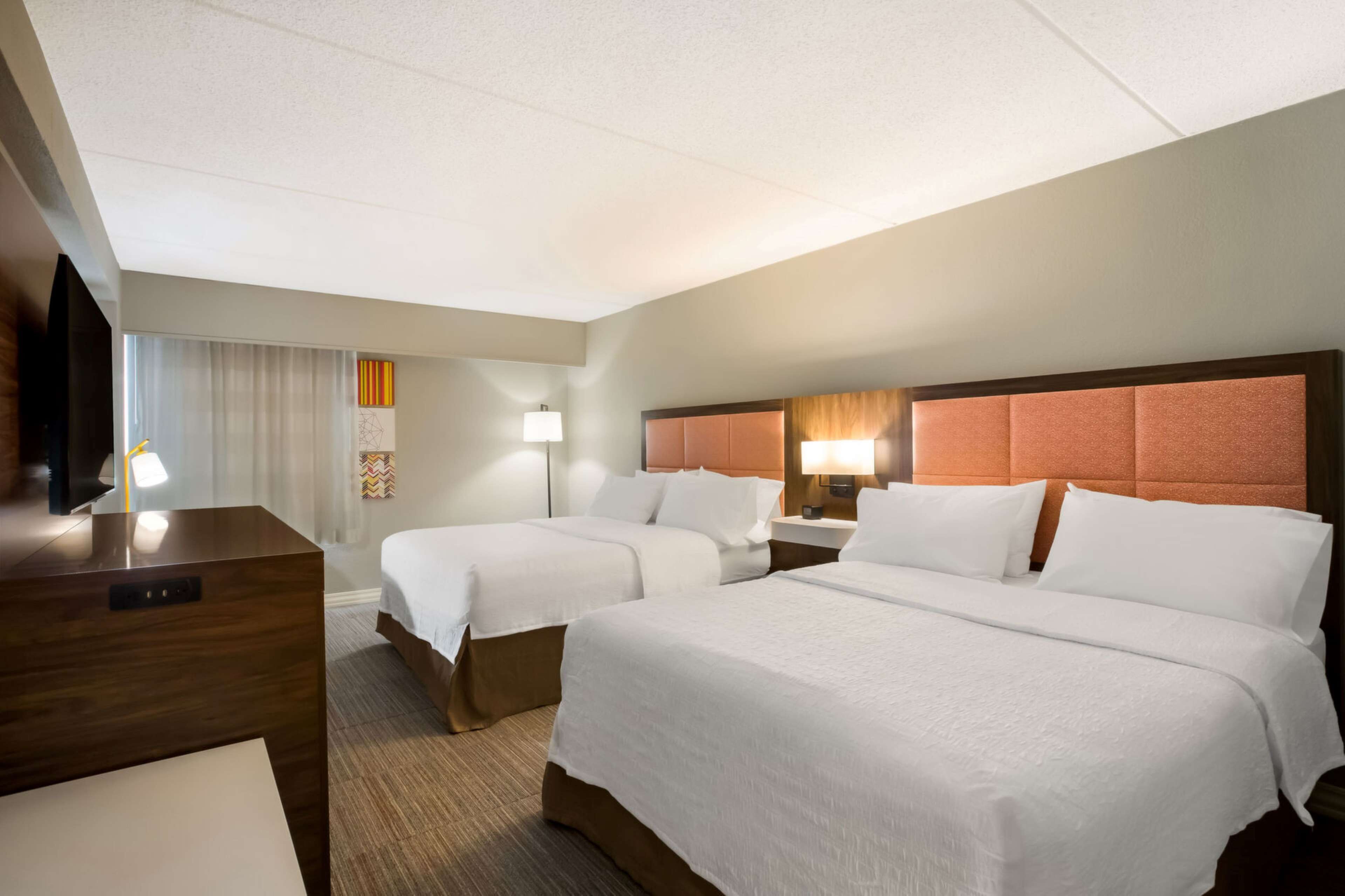 Une chambre d’hôtel avec deux lits, un bureau, une télévision et une fenêtre avec des rideaux.