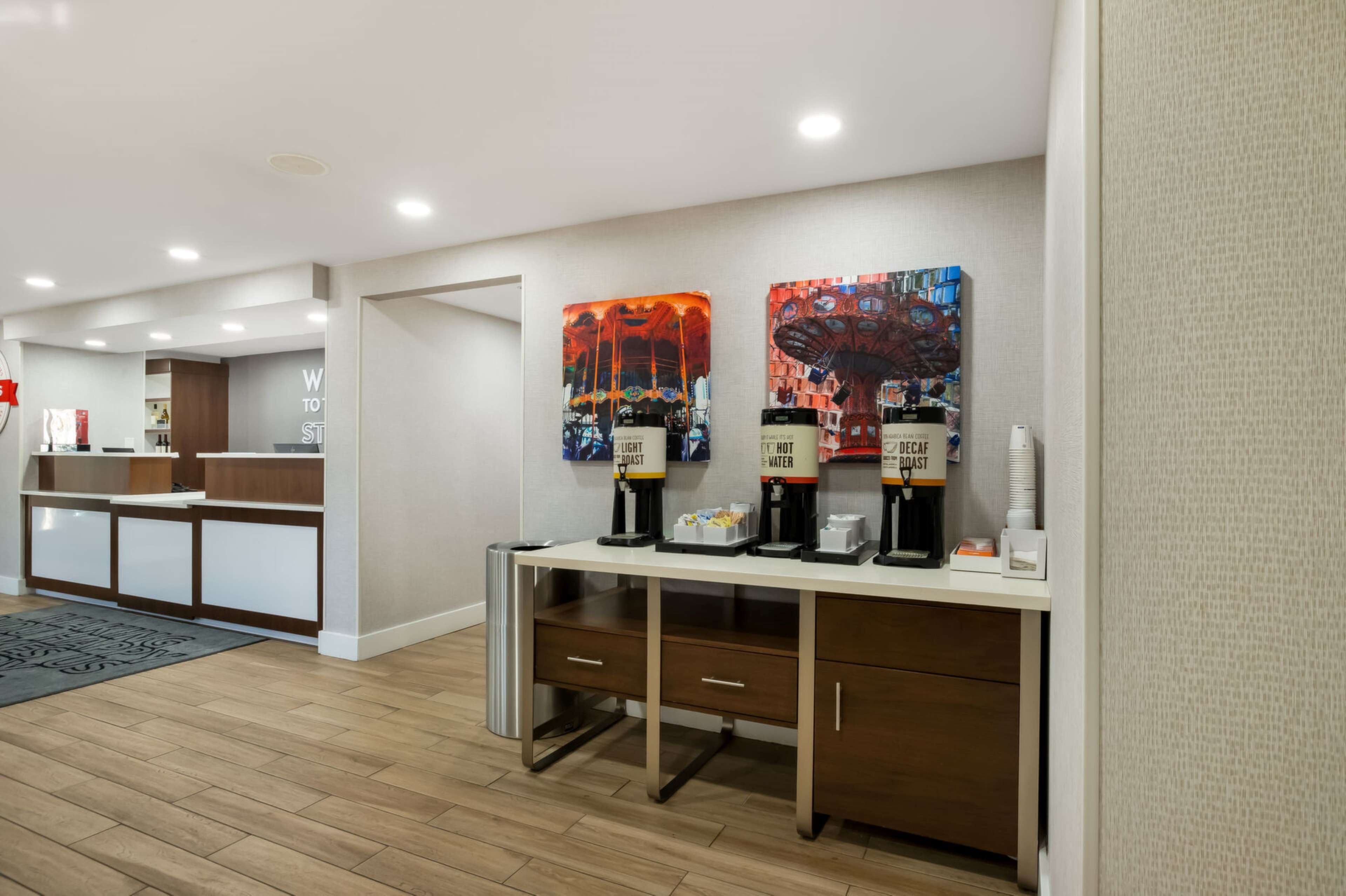 Een hotel receptie met een balie, koffieautomaten en kunstwerken aan de muur.