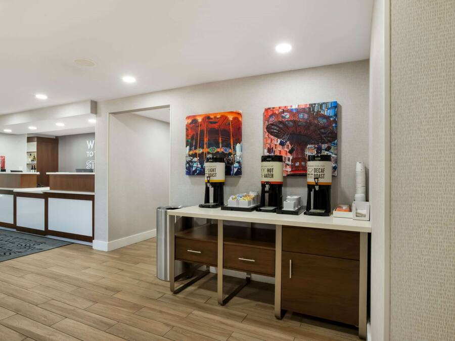 Ein Hotel-Rezeptionsbereich mit Empfangstresen, Kaffeeautomaten und Kunstwerken an der Wand.