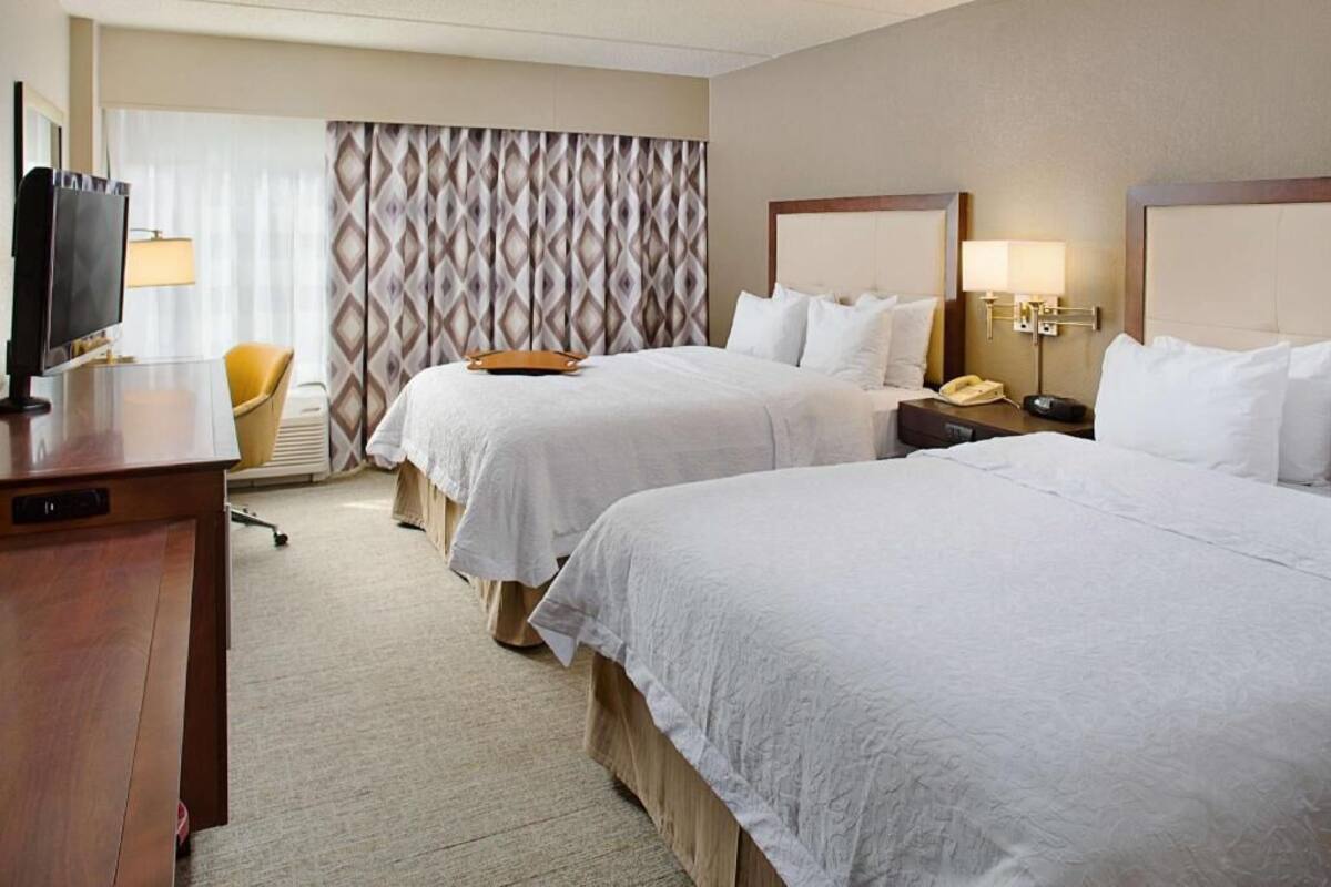 A hotel room with two beds, a desk with a TV, a chair, and a lamp.