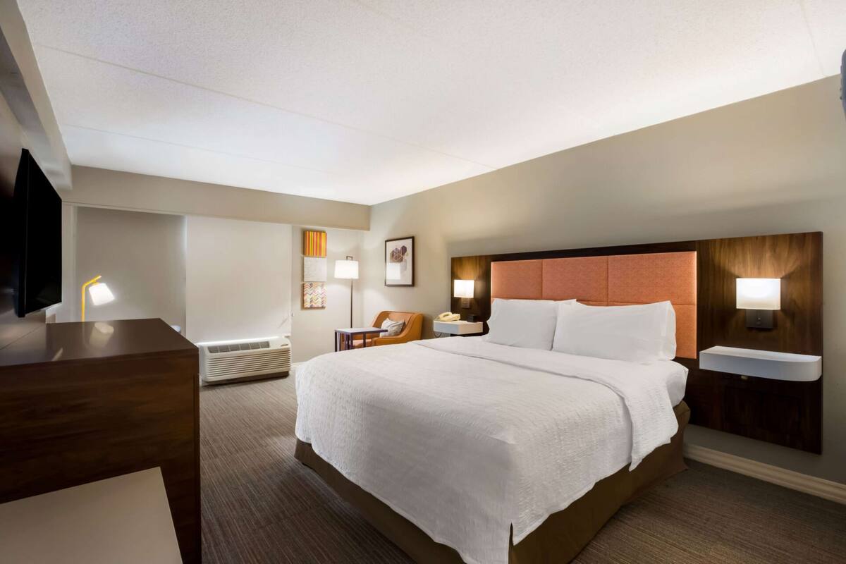 A hotel room with a large bed, bedside tables, a desk, and a TV.