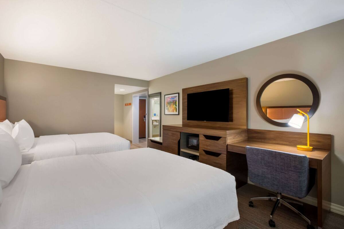 A hotel room with two beds, a desk, a television, a mirror, and a lamp.