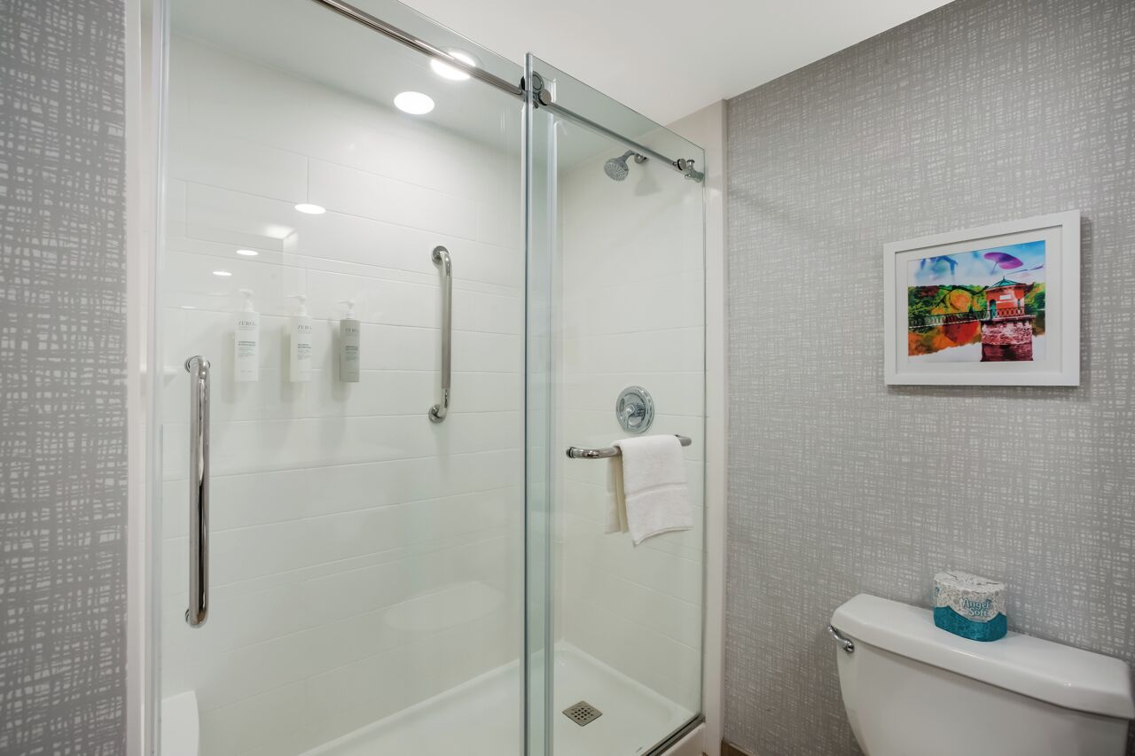 A modern bathroom with a glass shower enclosure, a toilet, and a framed picture on the wall.
