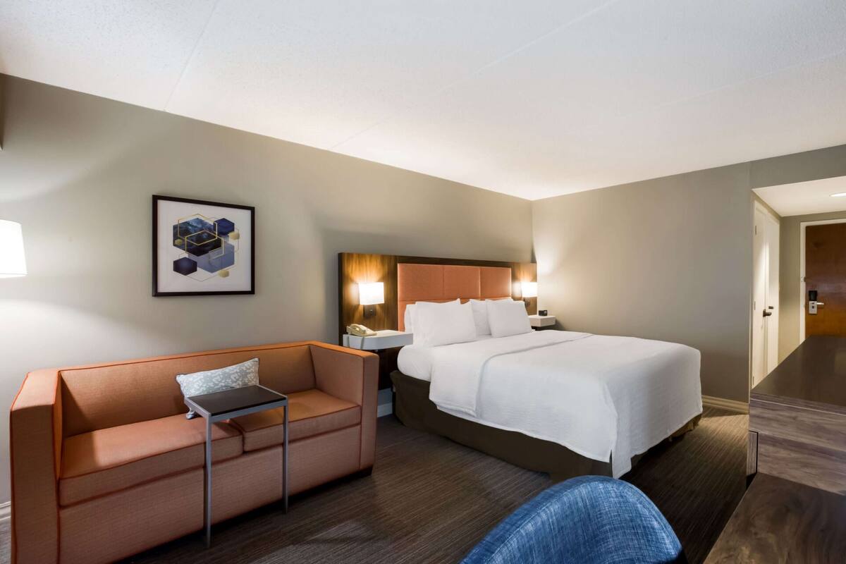 A hotel room with a bed, a sofa, a small table, and a nightstand with a lamp.