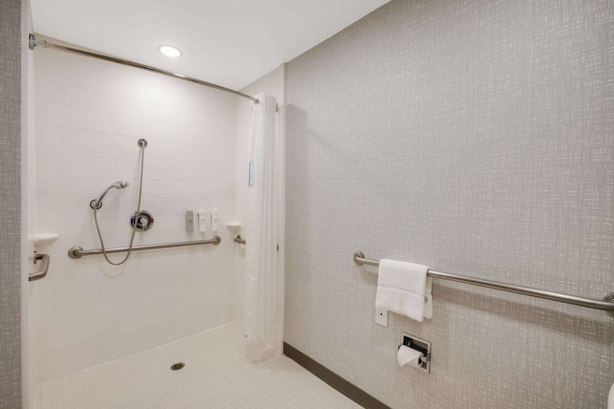 A bathroom with a shower, grab bars, a towel rack, and a toilet paper holder.