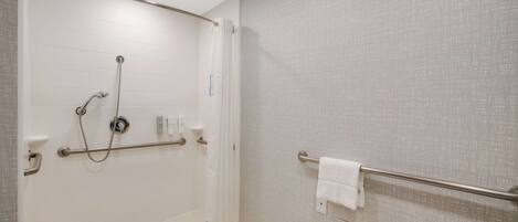 A bathroom with a shower, grab bars, a towel rack, and a toilet paper holder.