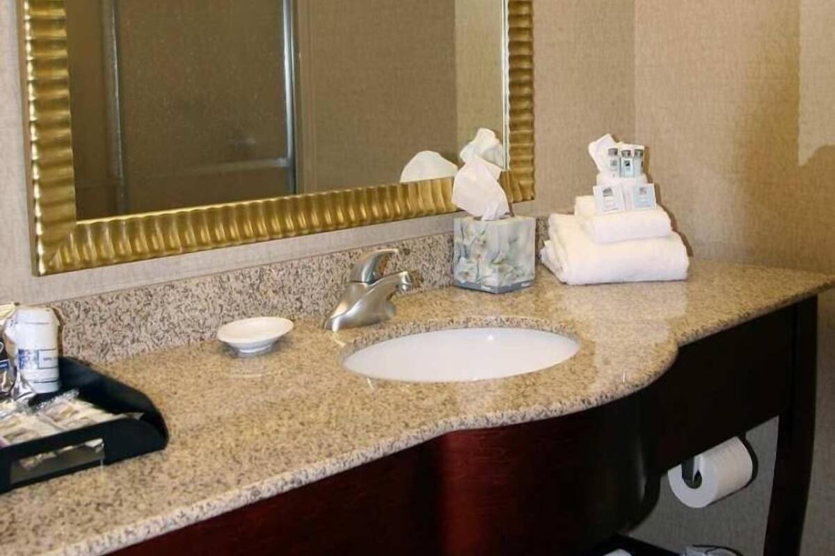 A bathroom with a granite countertop, a sink, a mirror, and a towel dispenser.