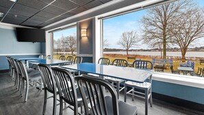 A conference room with a large table and chairs, a television, and a view of a park with trees and a body of water.