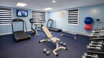 A gym with treadmills, a bench, dumbbells, and a television on the wall.