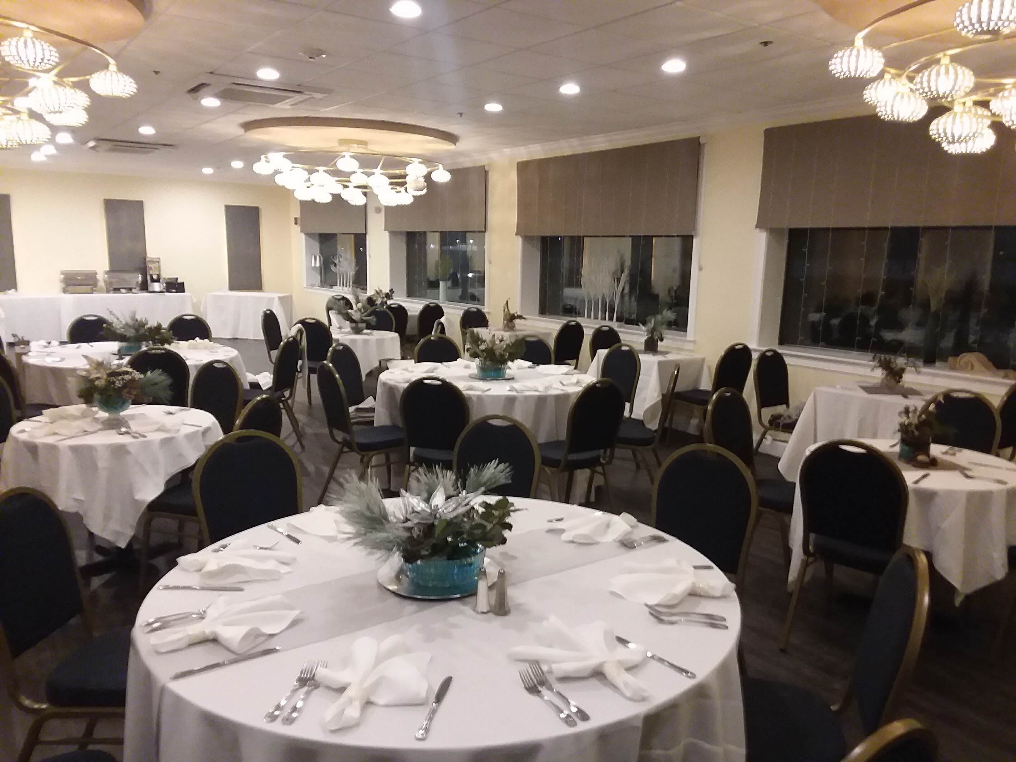 A banquet hall with round tables set for dining, each with white tablecloths and centerpieces.